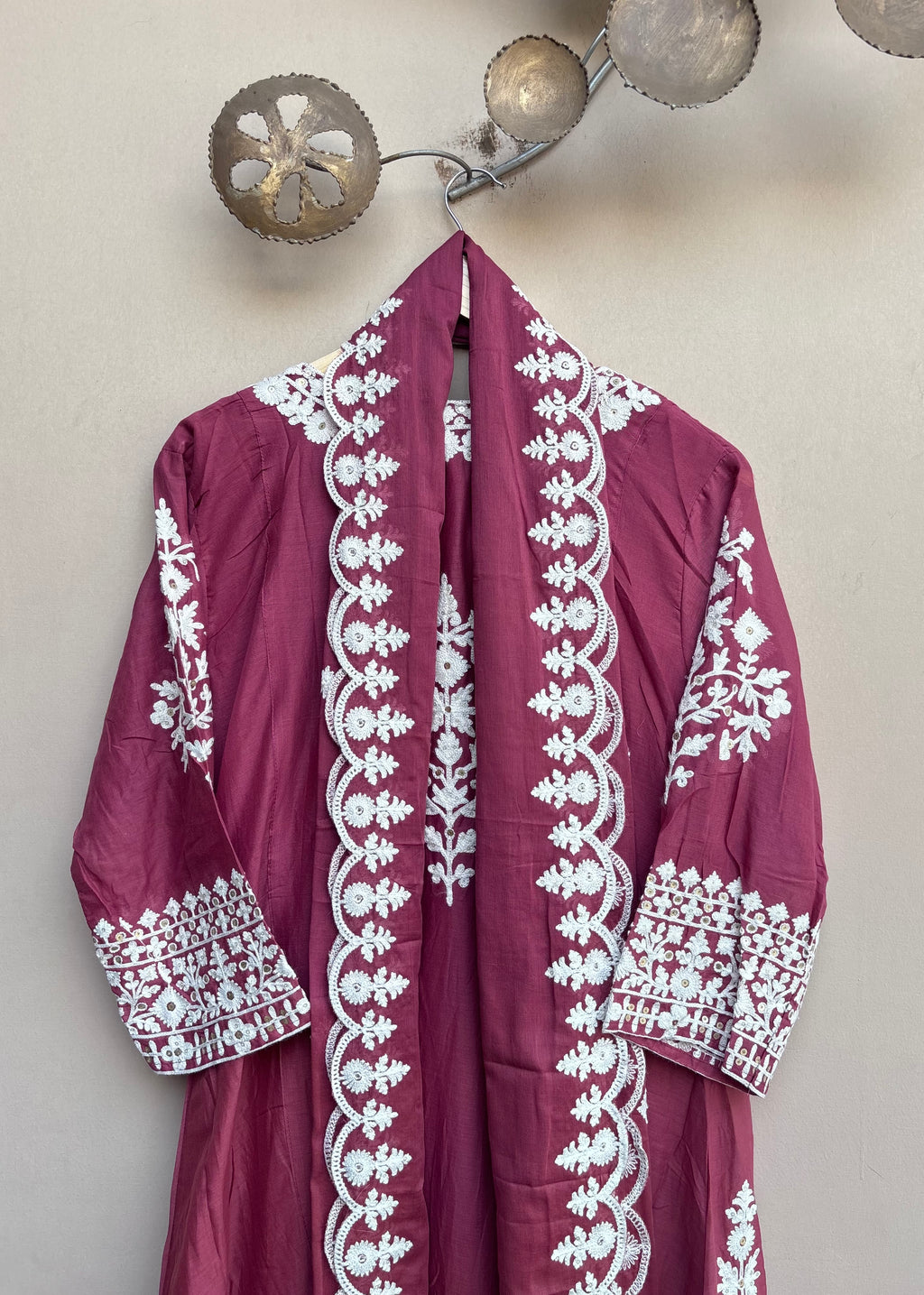 A magenta-pink traditional robe with intricate white embroidery hanging on a wall hook.
