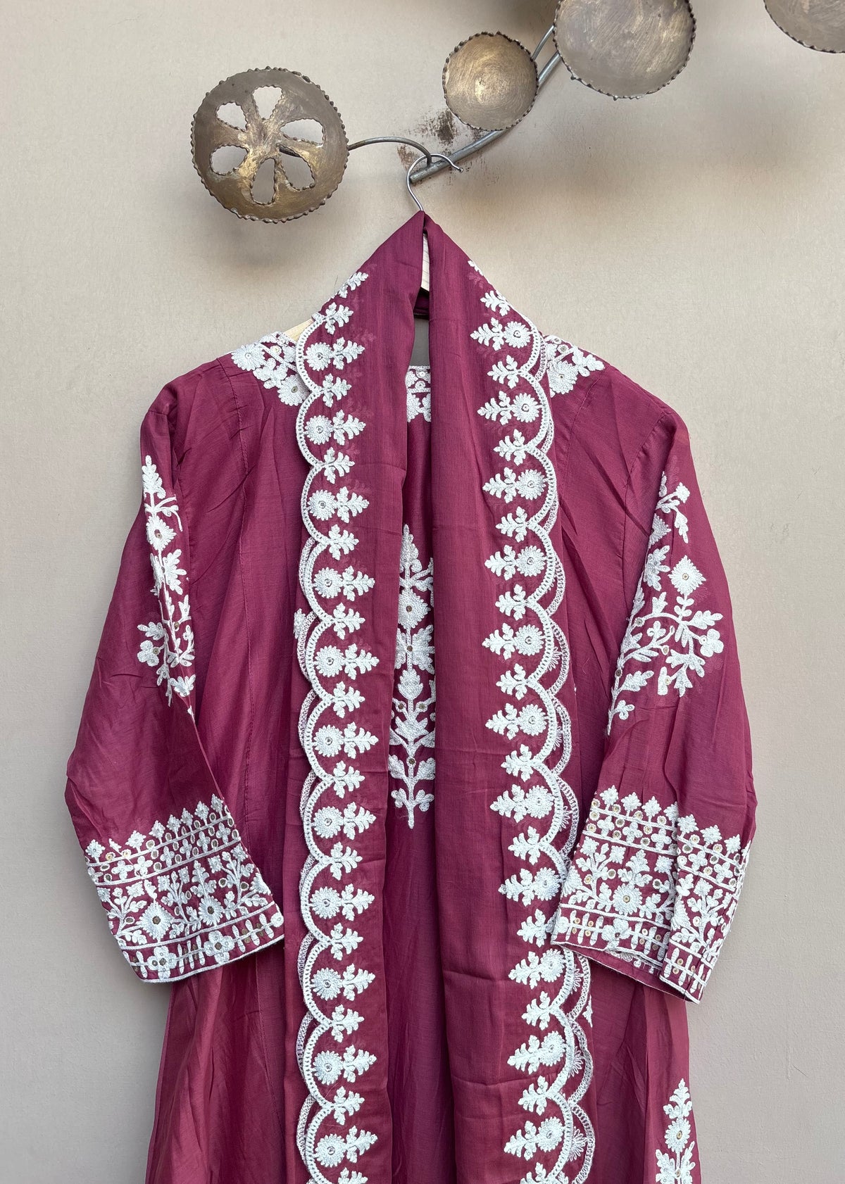 A magenta-pink traditional robe with intricate white embroidery hanging on a wall hook.