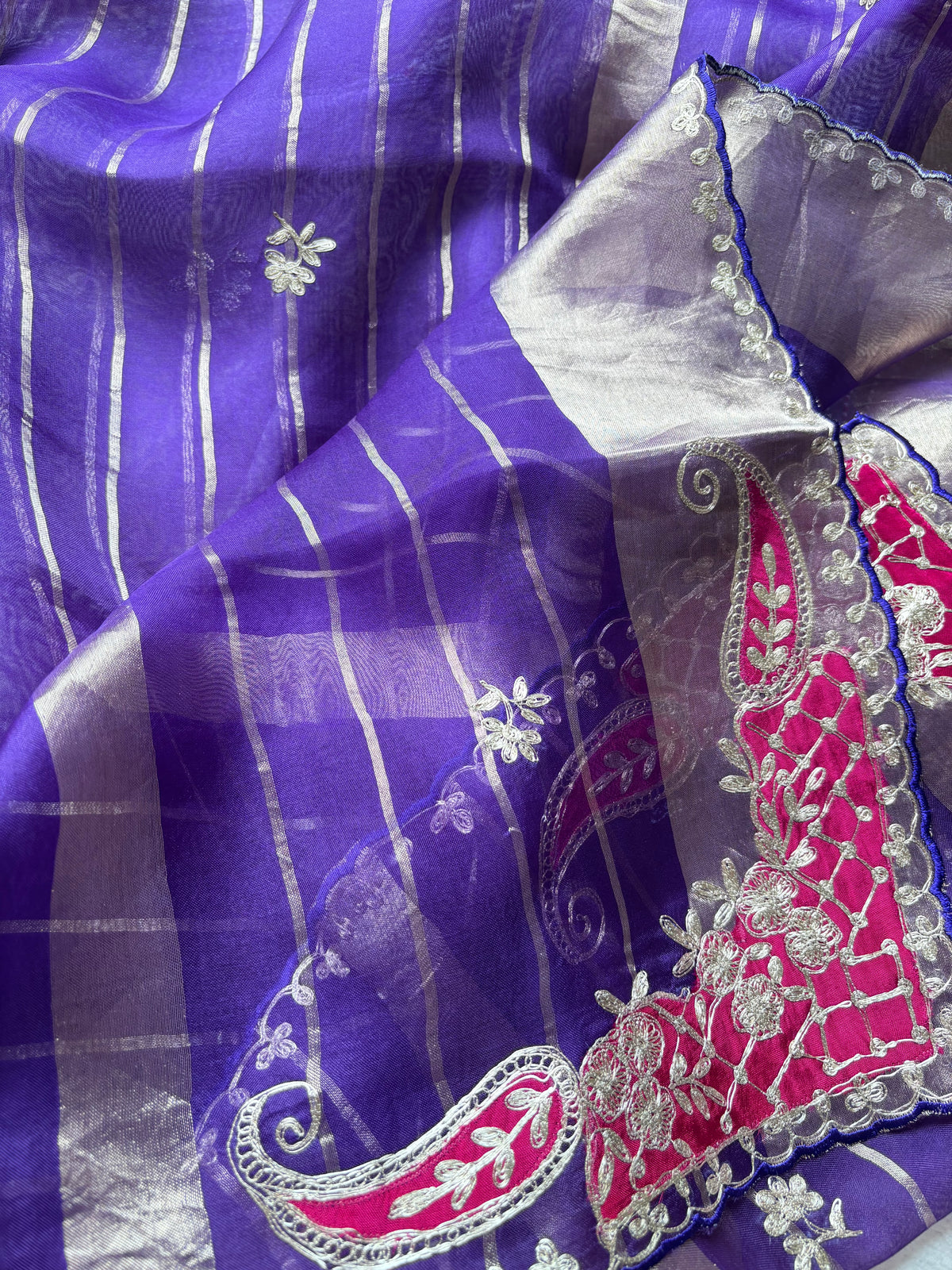A close-up of a purple and silver striped saree fabric with a bright pink and silver embroidered border.