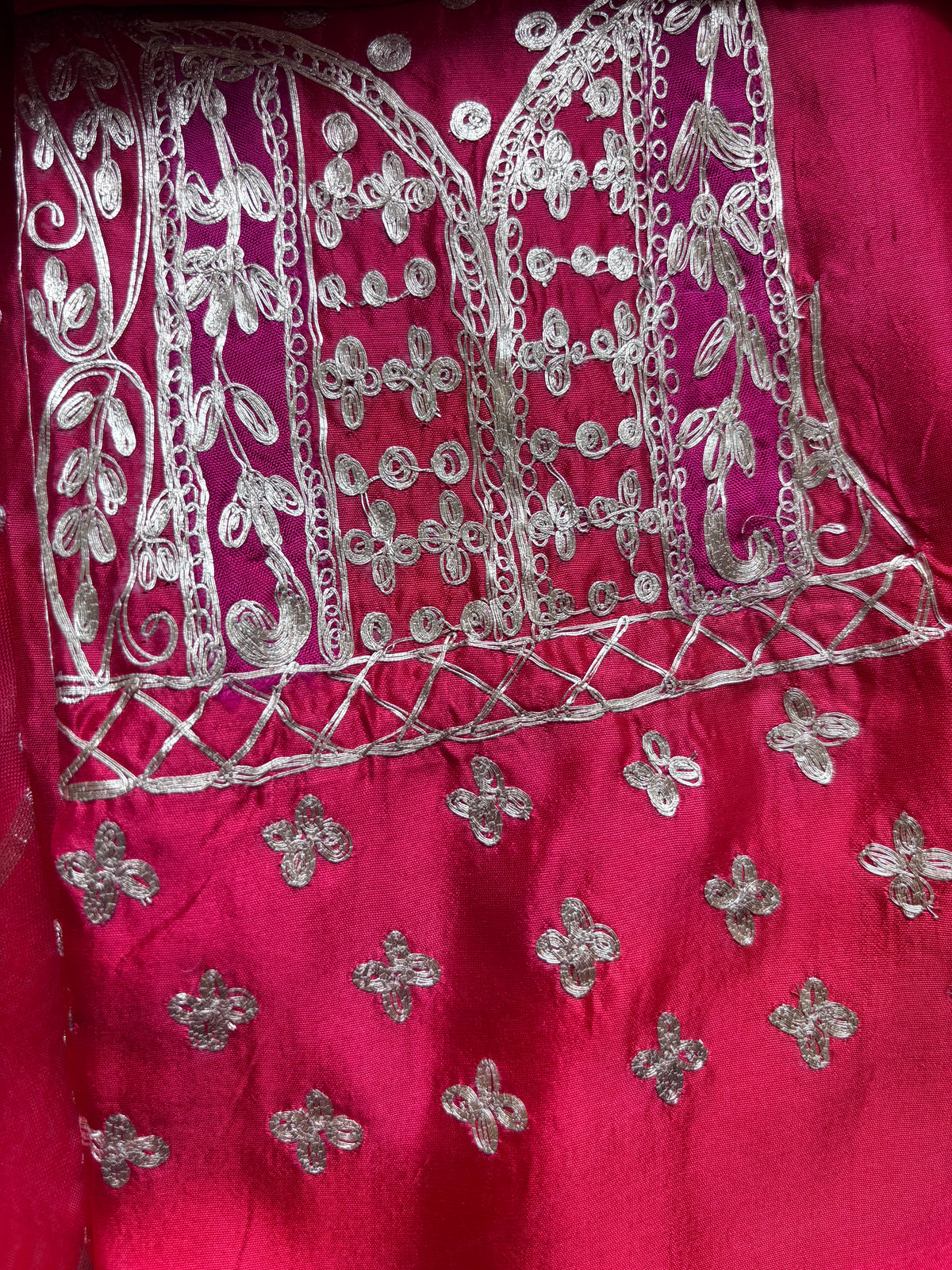 A close-up of a bright magenta pink fabric garment featuring intricate silver metallic embroidery and floral motifs.