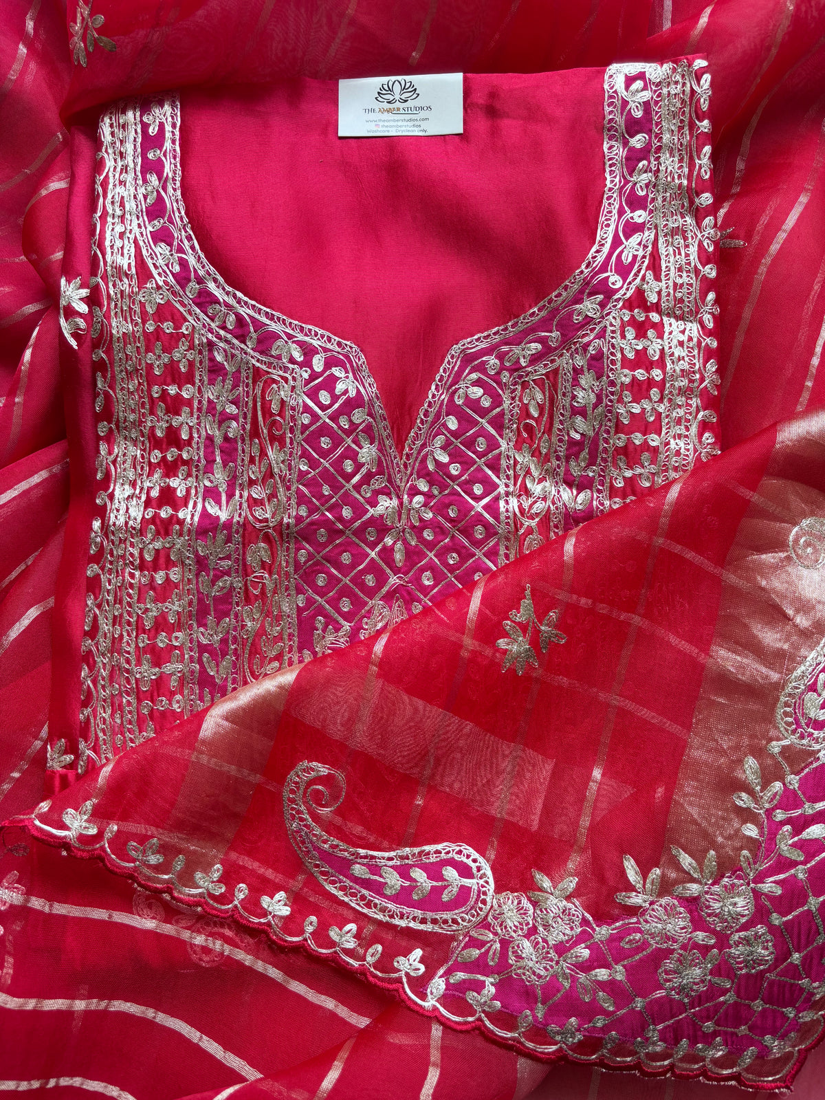 A close-up of a bright pink traditional outfit fabric set with intricate silver embroidery and a matching sheer dupatta featuring a paisley pattern.