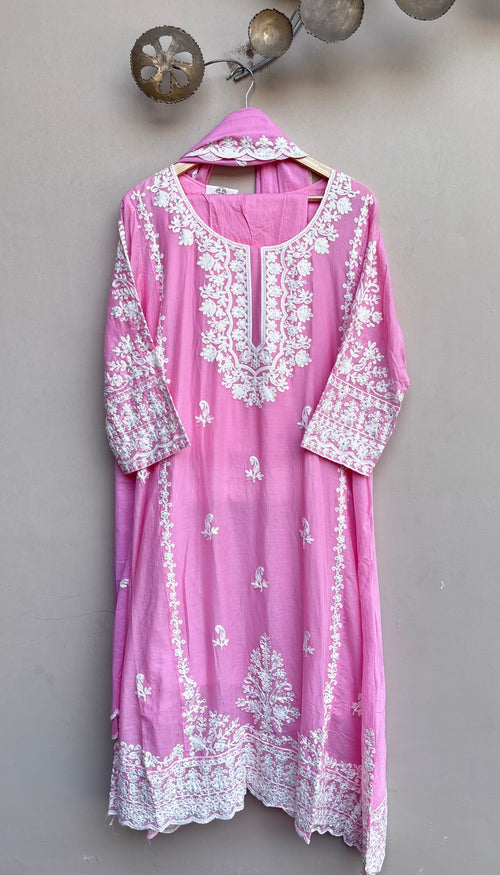 A pink traditional kurta with intricate white floral embroidery, hanging on a wooden hanger against a textured gray wall.