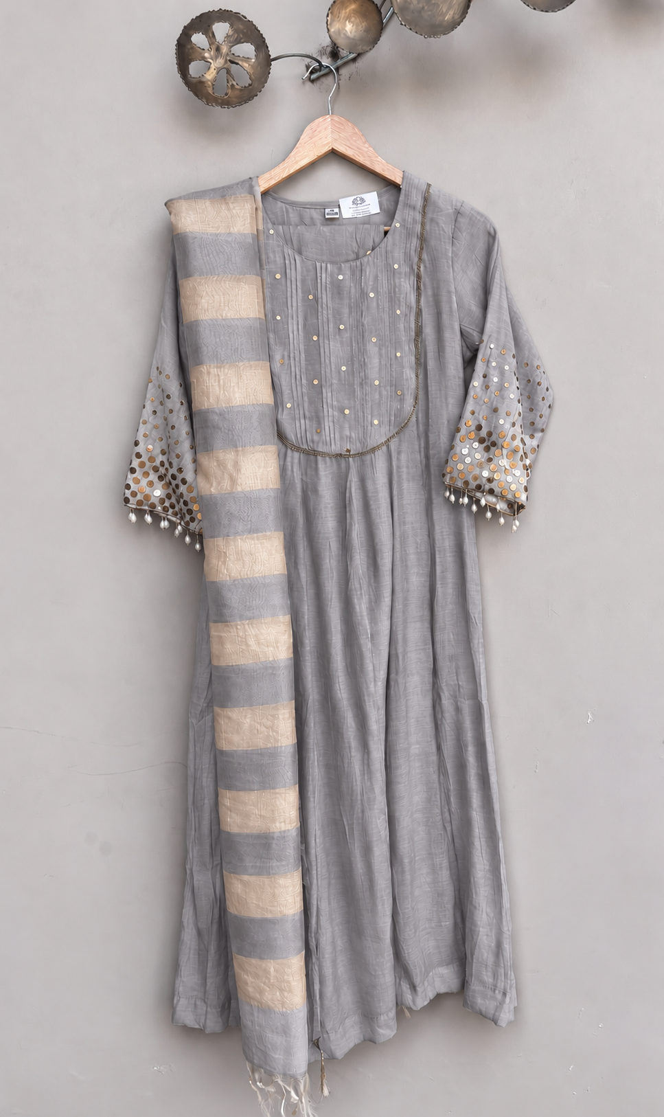 A grey-colored cotton kurta with a matching striped scarf draped over one shoulder, hanging on a wooden hanger against a dusty lavender wall.