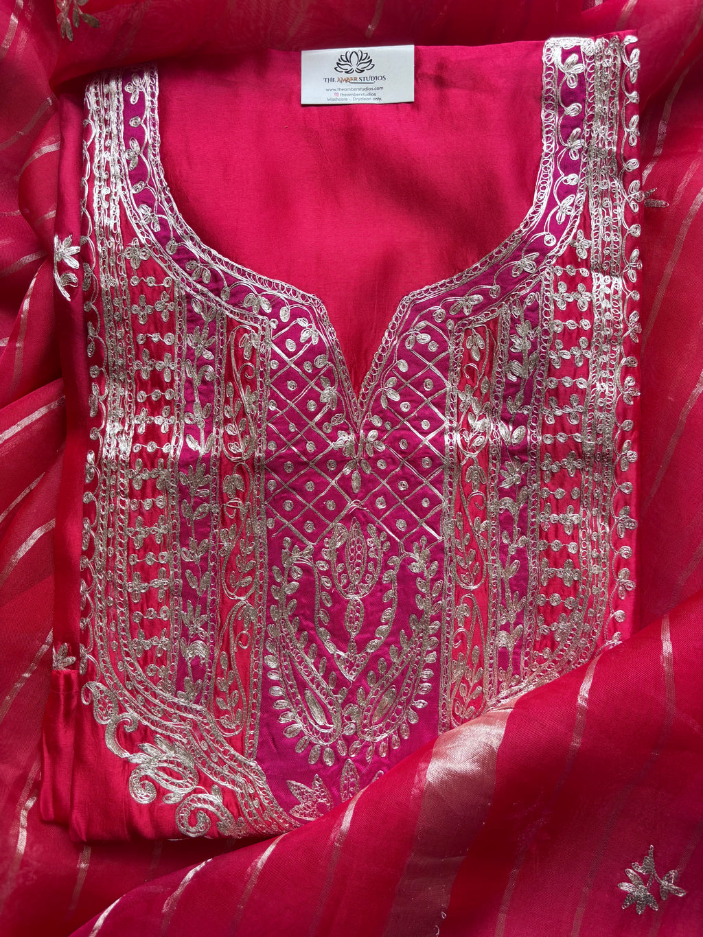 A close-up of a bright pink fabric garment, likely a kurta or blouse panel, featuring extensive silver mirror embroidery and a matching pink striped dupatta.
